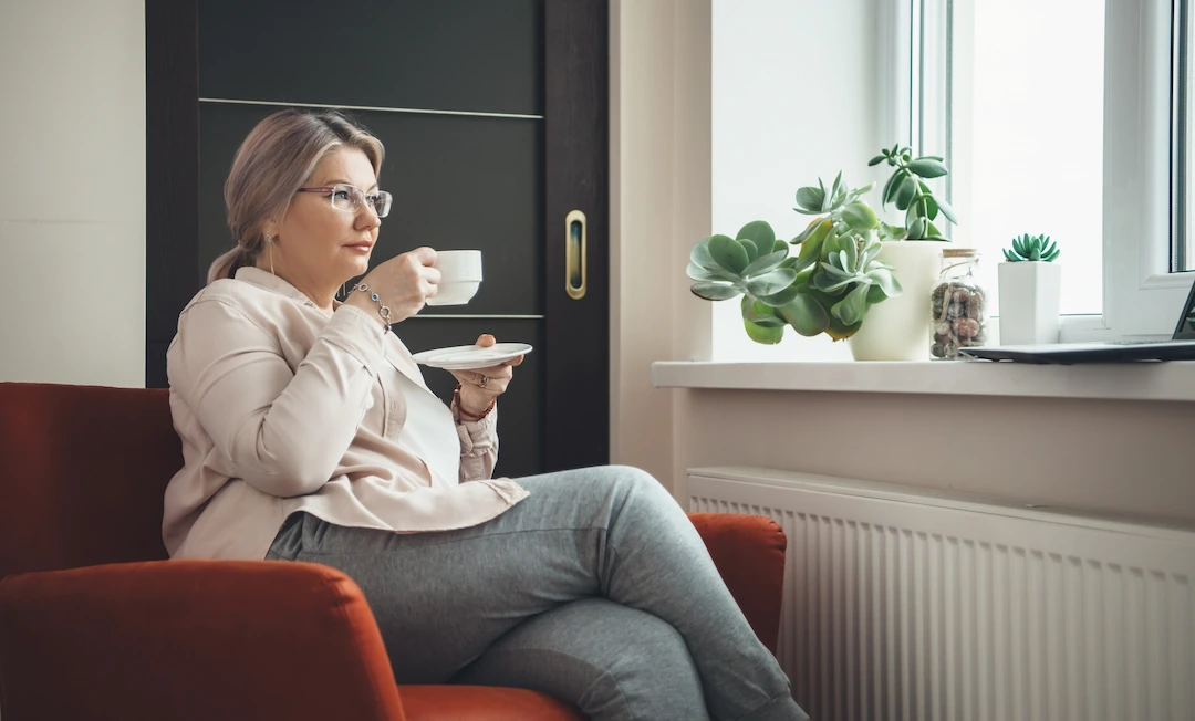 Middle-aged woman looking out window drinking coffee